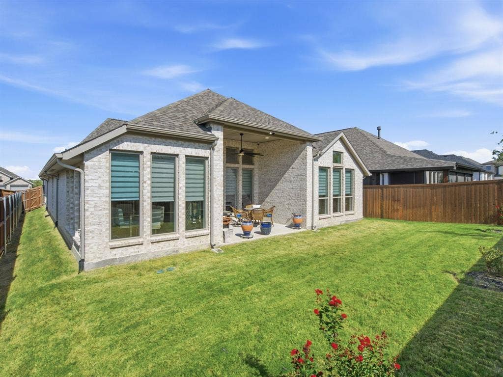 Expansive backyard featuring a manicured lawn, a covered patio, and a light-colored brick exterior