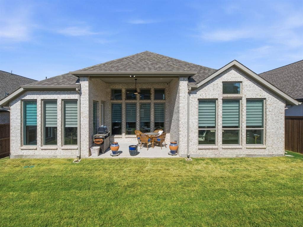 Brick exterior with multiple large windows, covered patio, outdoor ceiling fan, and a spacious green lawn