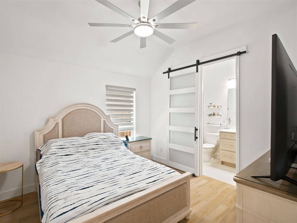 Vaulted ceiling with an integrated ceiling fan, wood-finish flooring, and a modern sliding barn door with frosted panels