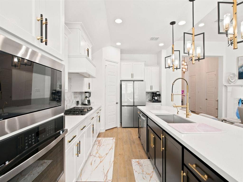 Modern kitchen featuring stainless steel appliances, white cabinetry, a kitchen island with seating, a gas cooktop, and brass-finish hardware
