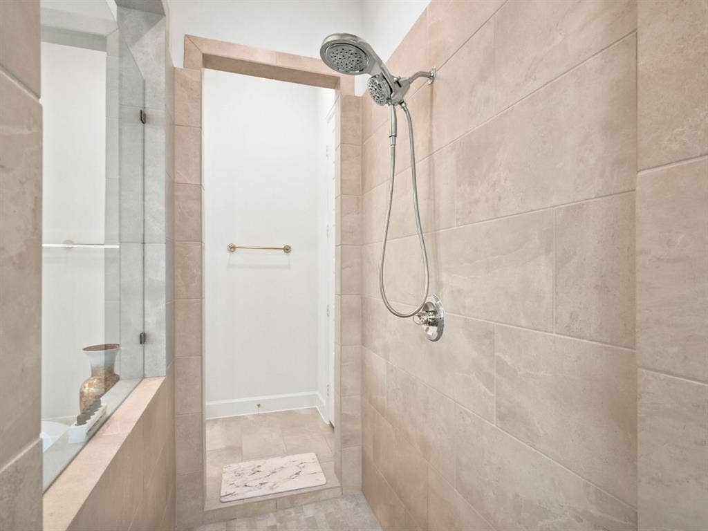 Tiled shower enclosure featuring a multi-function showerhead, polished chrome fixtures, and a glass partition