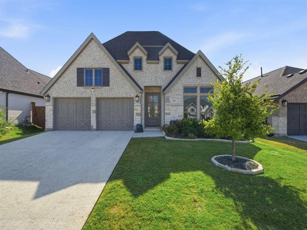 Stone and brick facade with dormer windows, a two-car garage, and a concrete driveway