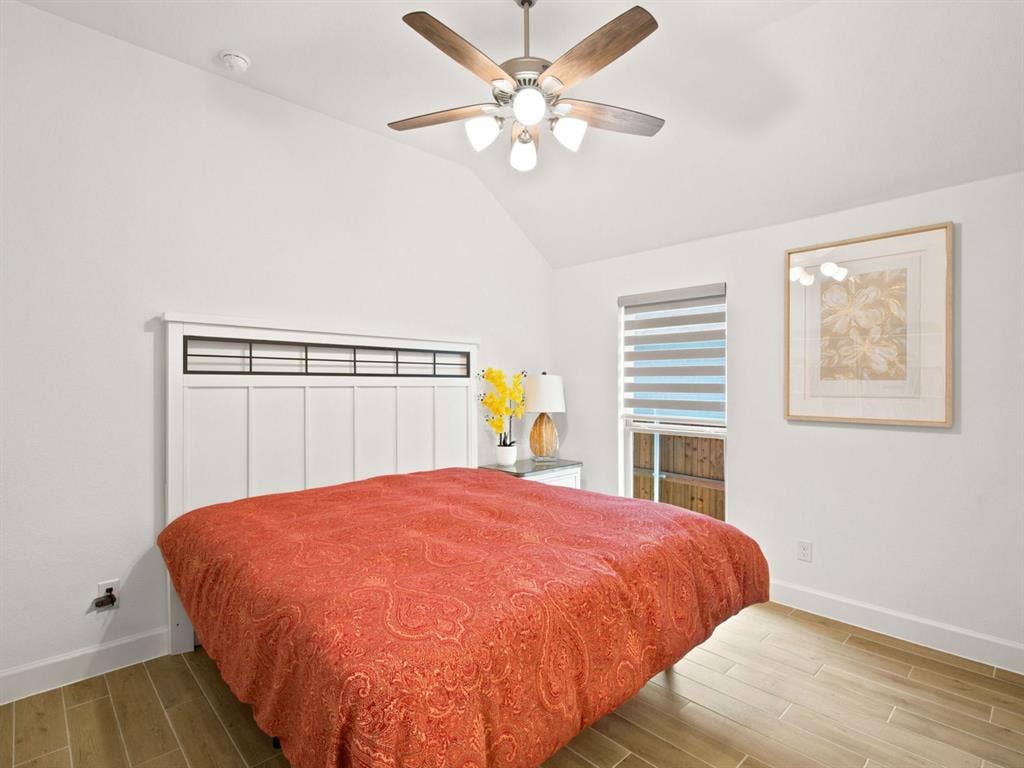 Vaulted ceiling with a ceiling fan and light fixture, wood-finish flooring, and a large window with privacy blinds