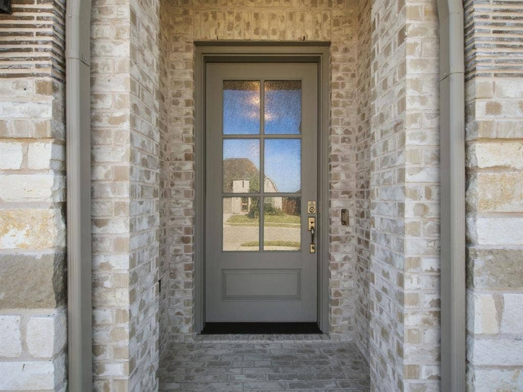Panel-style front door with decorative glass inserts, framed by brick and stone veneer