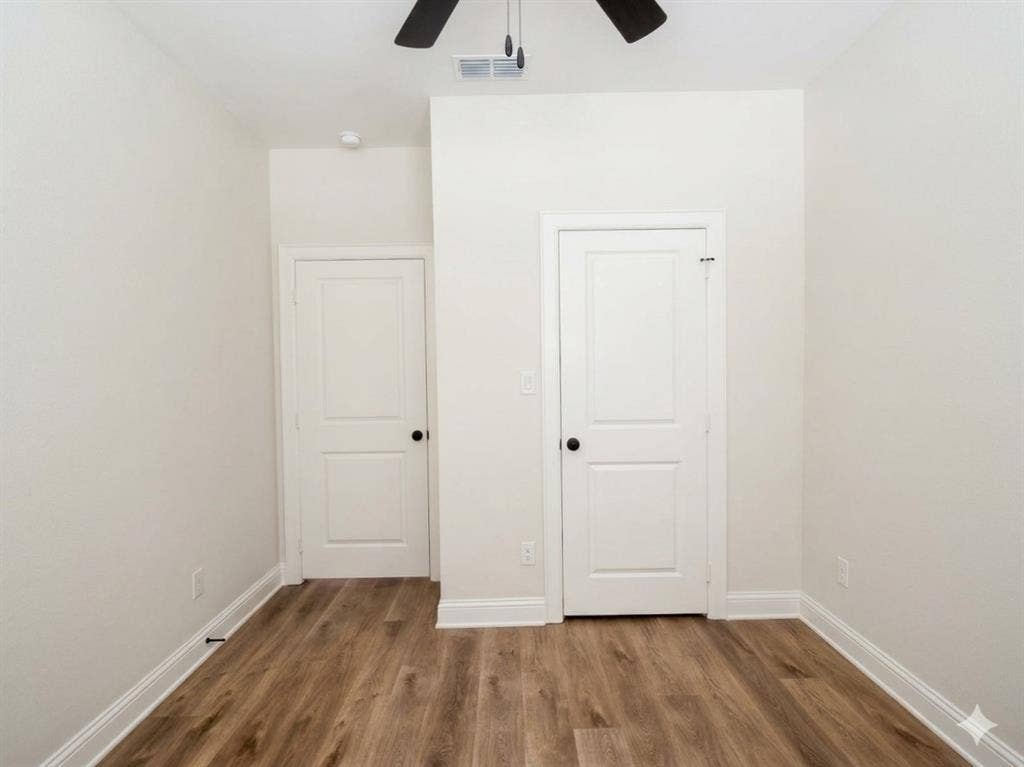 11034 Oak Springs Cove, Tyler, TX 75703 Wood-finish flooring, white paneled doors with black hardware, ceiling fan with black blades, white baseboards, and neutral wall tones
