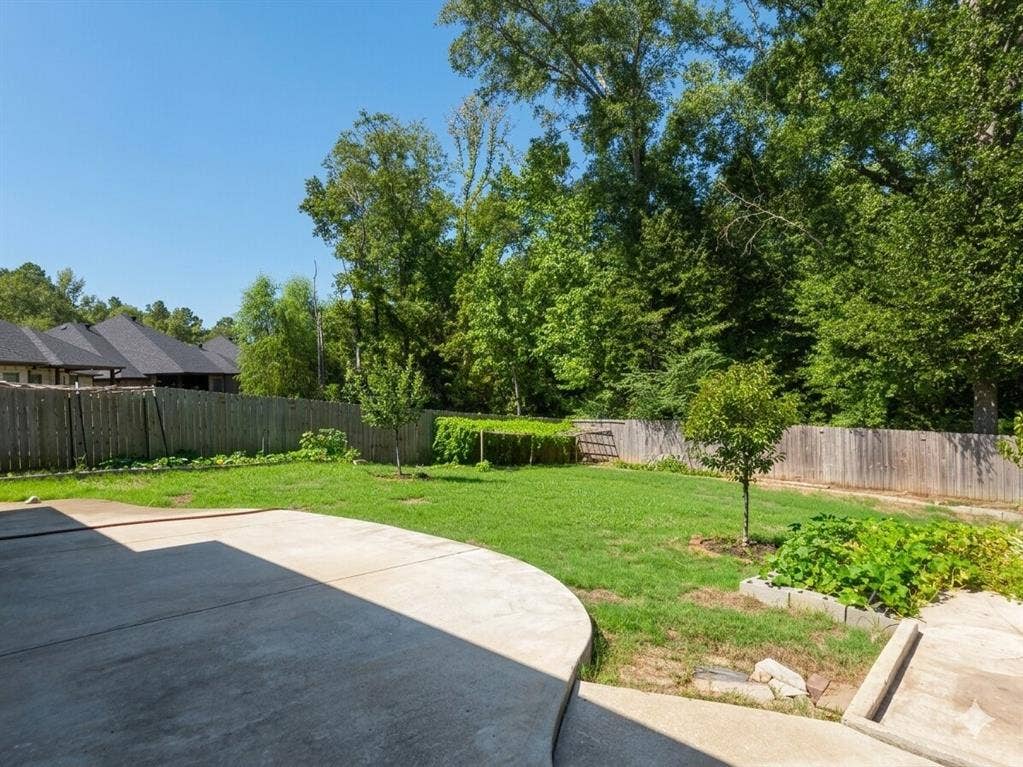 11034 Oak Springs Cove, Tyler, TX 75703 Expansive concrete patio with a manicured lawn, surrounded by a wood privacy fence and mature trees