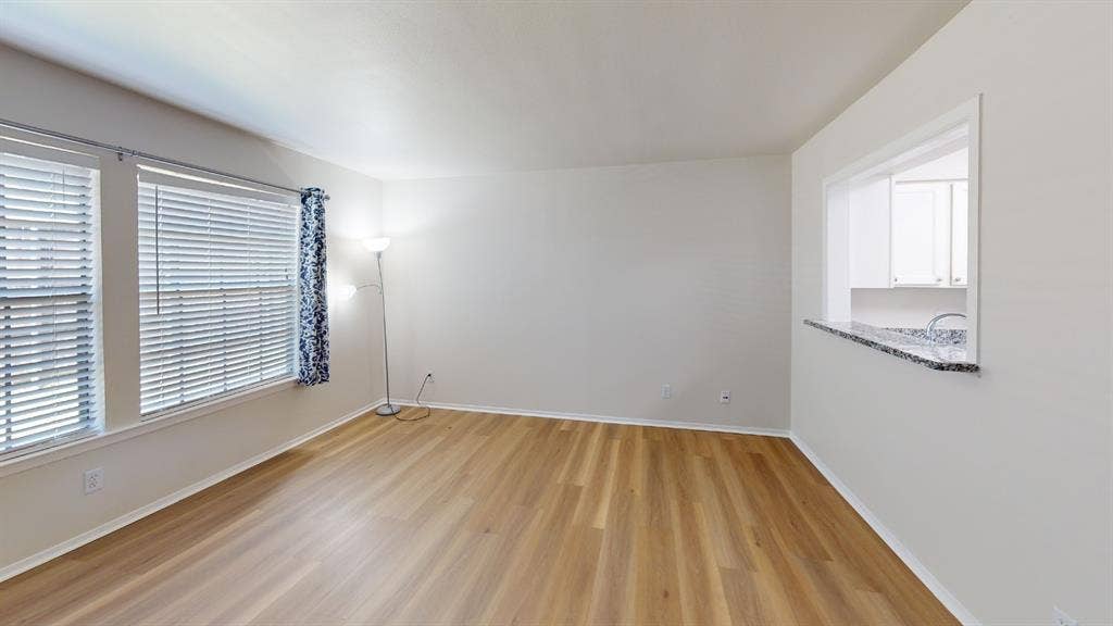 5335 Bent Tree Forest Drive, #150, Dallas, TX 75248 Expansive room featuring wood-finish flooring, two windows with horizontal blinds, and a pass-through opening with a granite-look countertop