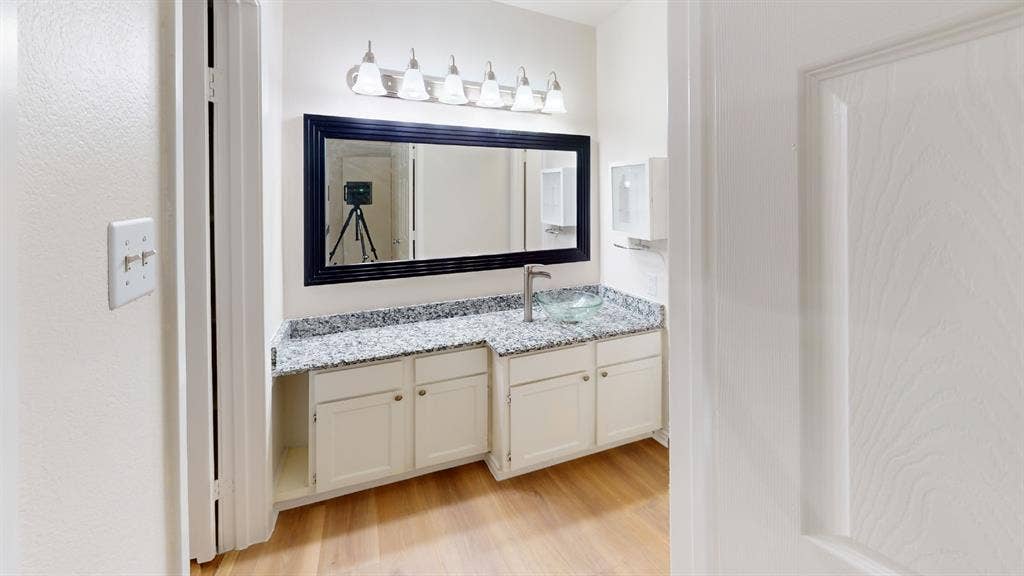 5335 Bent Tree Forest Drive, #150, Dallas, TX 75248 Vanity with a framed mirror, granite-finish countertop, under-sink cabinetry, and wood-finish flooring