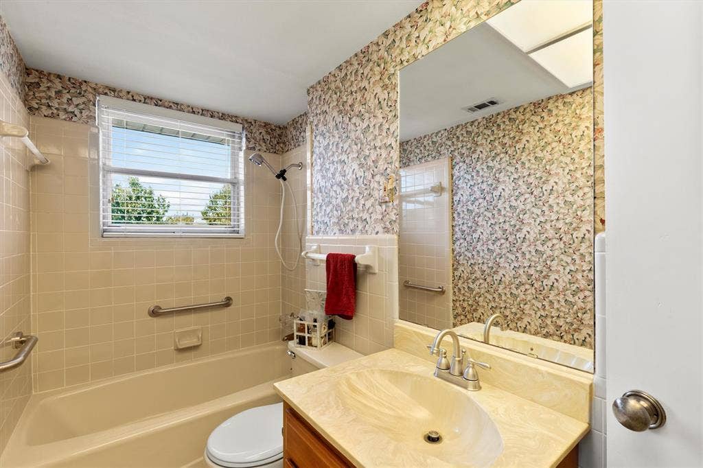 1013 Bandera Lane, Garland, TX 75040 Tub/shower combination with grab bars, wood-finish vanity with countertop sink, wall-mounted mirror, and window with blinds