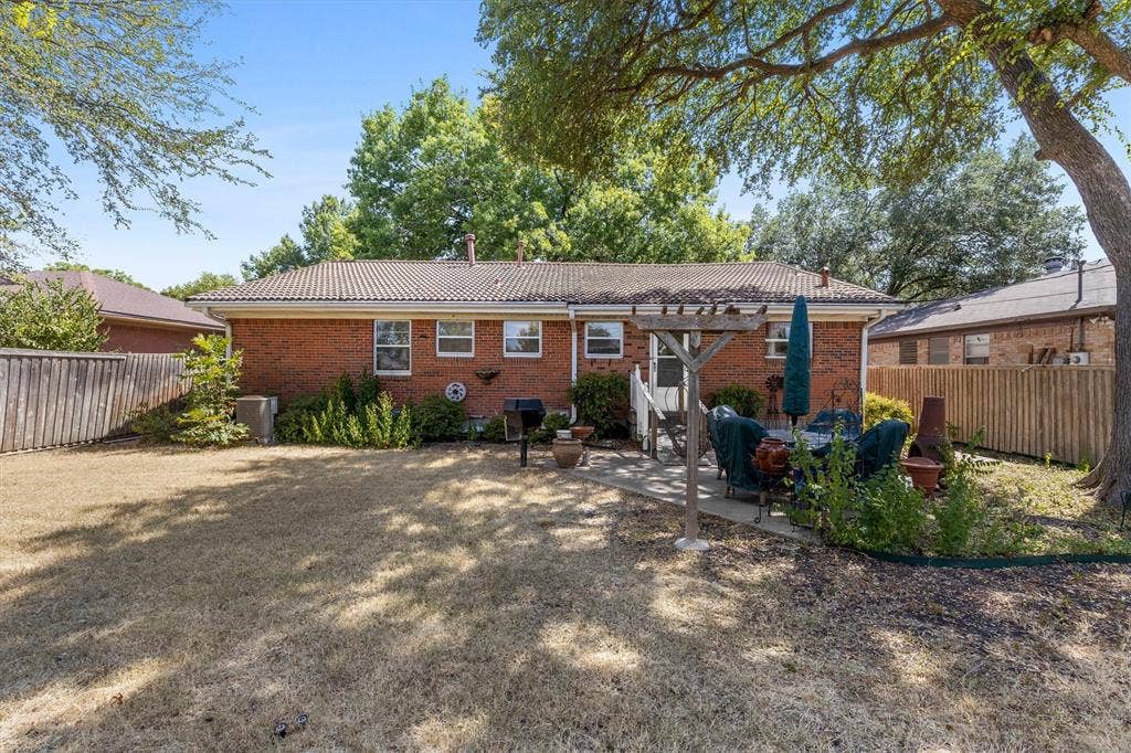 1013 Bandera Lane, Garland, TX 75040 Brick exterior with a tiled roof, multiple windows, and a paved patio area