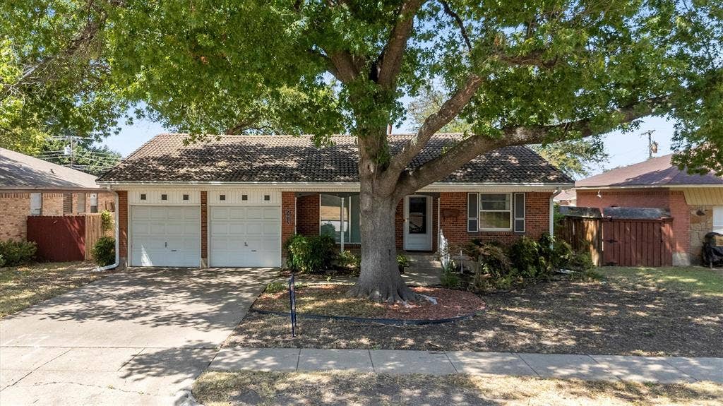 1013 Bandera Lane, Garland, TX 75040 Brick exterior with a tiled roof, two-car garage, and established front yard tree