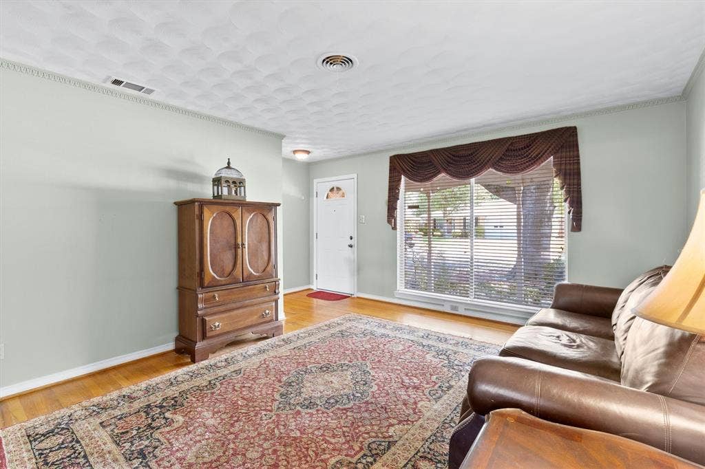 1013 Bandera Lane, Garland, TX 75040 Hardwood flooring throughout, crown molding, large picture window with blinds, front entry door with decorative glass insert, and a textured ceiling