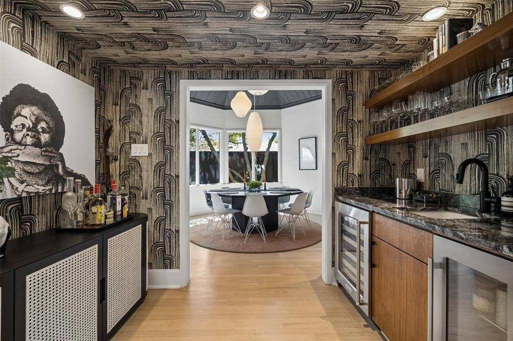 A stylish wet bar with wine and beverage refrigerators and Kelly Wearstler wallpaper leads to the dramatic formal dining room.