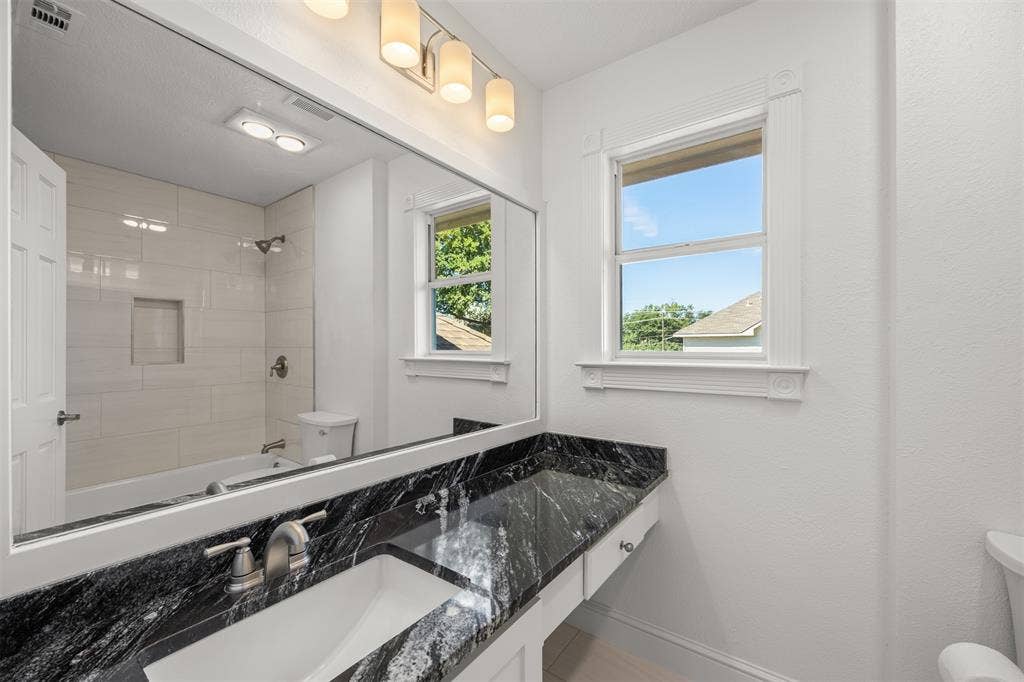 4203 N Capistrano Drive, Dallas, TX 75287 Upstairs hall bathroom has granite countertop, new sink with brushed nickel faucet, new tub and shower with brushed nickel faucets. New tile has been installed surrounding the tub area and on floors. A new Kohler toilet along with new lighting fixtures have been installed. The tub surround tile and floor are white.