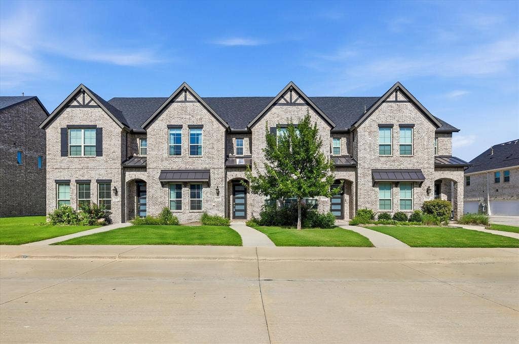 12952 Wymeth Drive, Farmers Branch, TX 75234 Modern townhome featuring light gray brick exterior, dark gabled rooflines, black window shutters and contemporary entry doors with frosted glass panels.