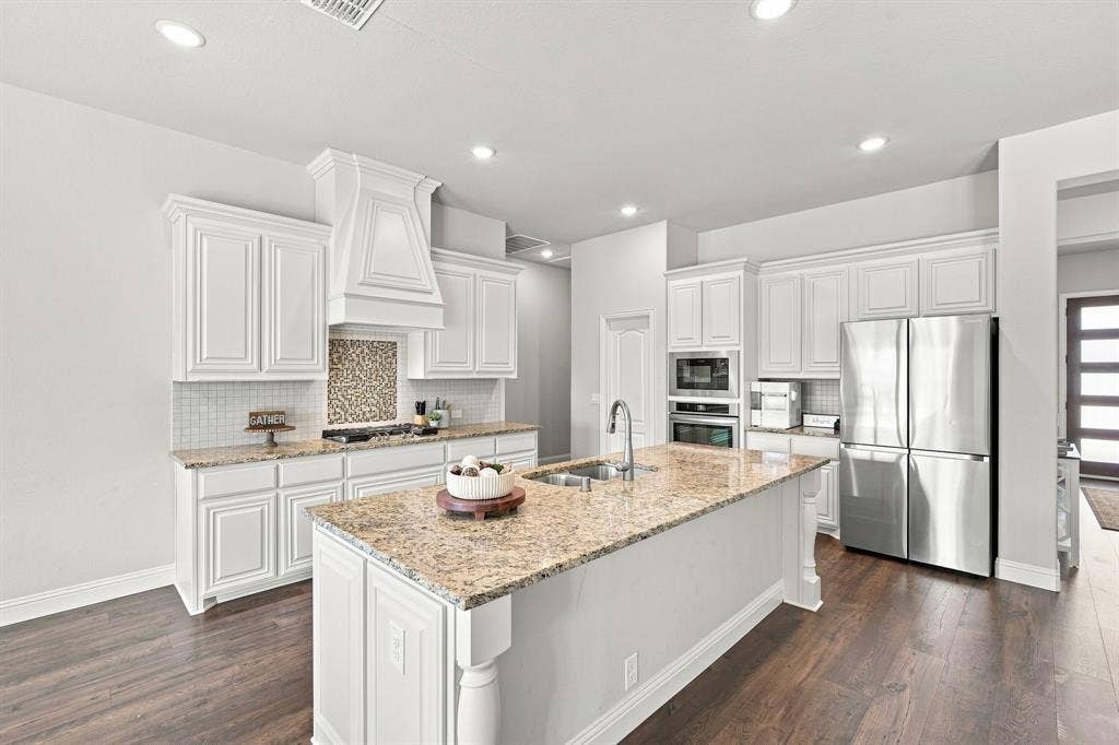 Equipped with built-in stainless steel appliances, a gas cooktop, a custom wood vent hood, and designer backsplash