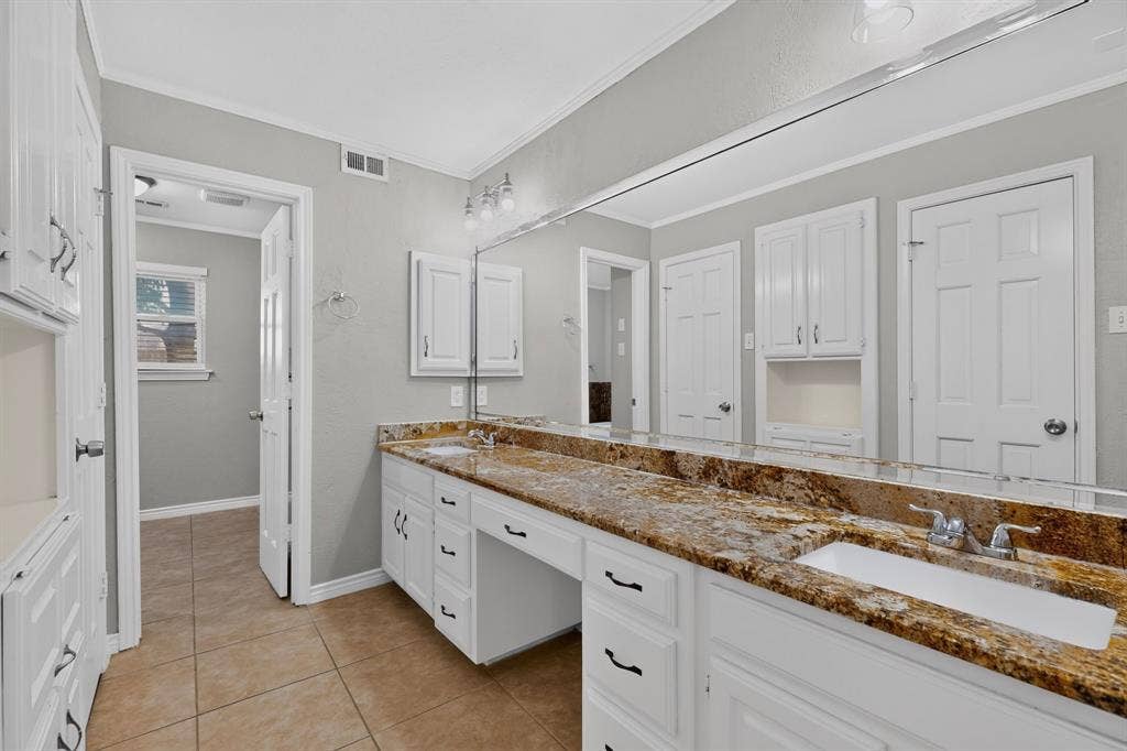Double vanity with integrated sinks, expansive countertop, white cabinetry, and tile flooring
