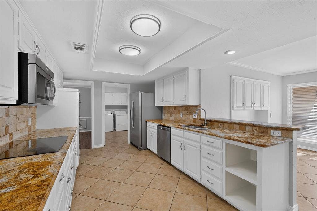 Kitchen featuring white cabinetry, stainless steel appliances, stone countertops, and tile flooring