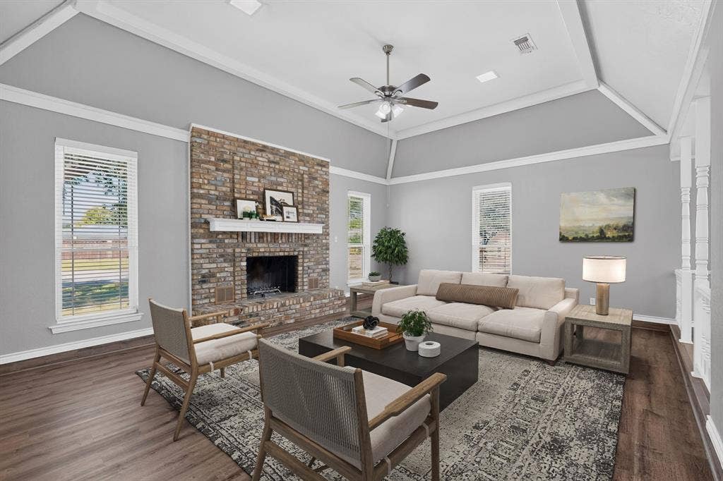 Spacious living area featuring a brick fireplace, wood-finish flooring, and a tray ceiling with a fan