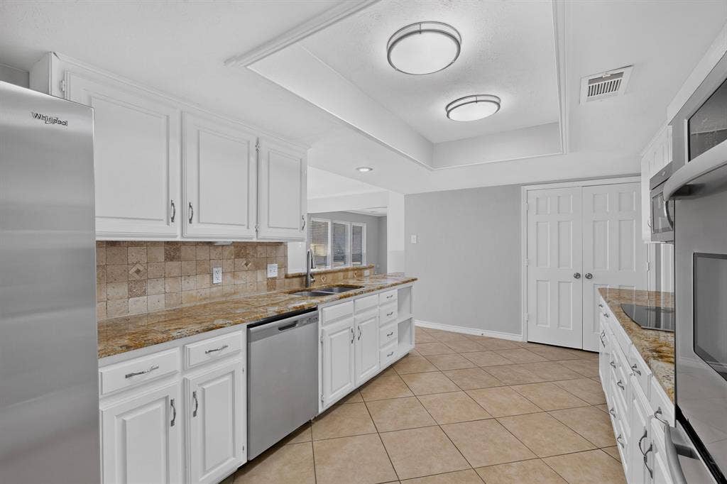 White cabinetry, stainless steel appliances, tile flooring, stone countertops, and a tile backsplash