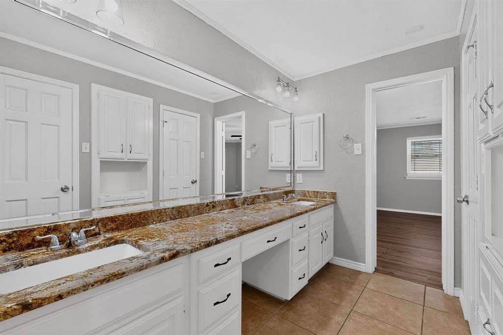 Dual sink vanity with stone-finish countertop, white cabinetry, and a full-width mirror