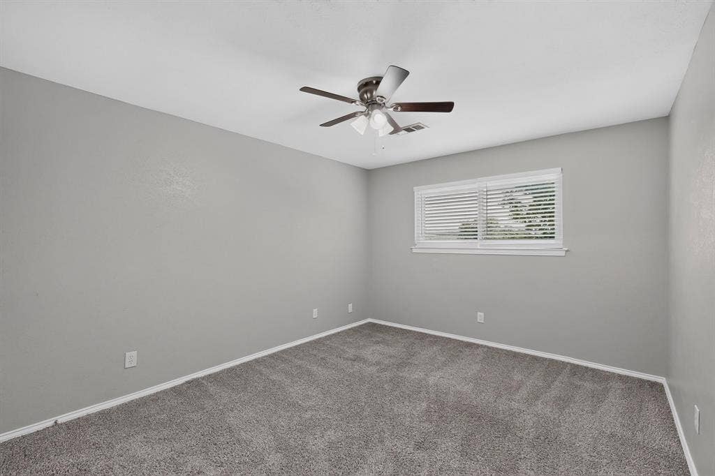 Gray carpeting and walls, a window with horizontal blinds, and a ceiling fan with integrated lighting