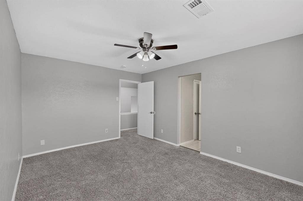 Neutral gray wall finish, gray carpet flooring, ceiling fan with light fixture, white trim, and white interior doors