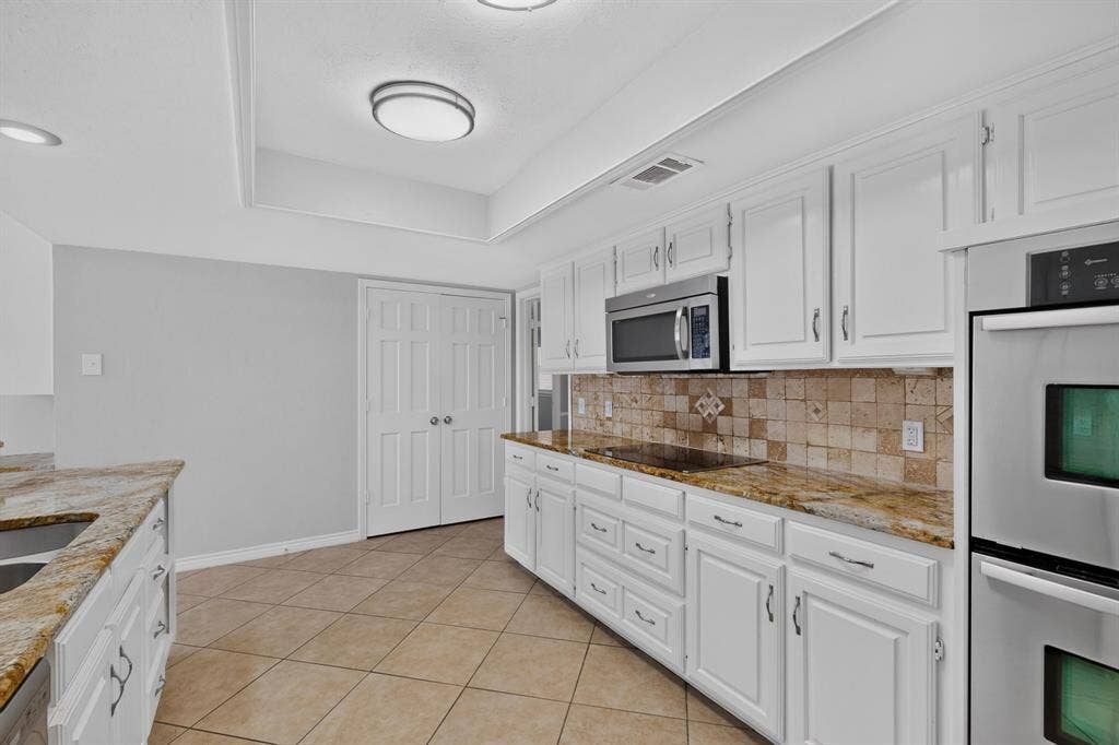 Kitchen featuring white cabinetry, tile flooring, granite countertops, tile backsplash, and stainless steel appliances