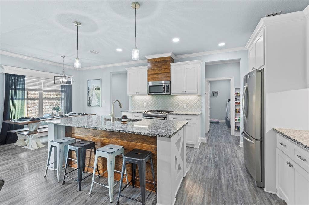 22477 County Road 2166, Troup, TX 75789 Kitchen featuring a large island with a stone counter, wood-finish flooring, white cabinetry, integrated stainless steel appliances, and a tiled backsplash