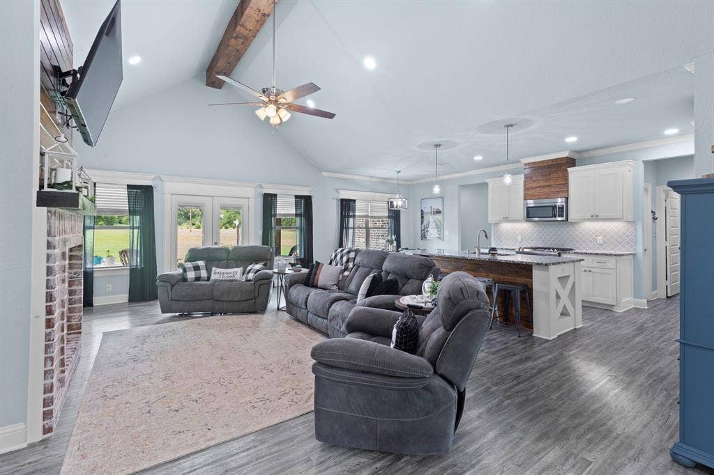 22477 County Road 2166, Troup, TX 75789 Vaulted ceiling with exposed wood beam, wood-finish flooring, brick fireplace with mantel, white cabinetry, and a kitchen island with a wood-wrapped base