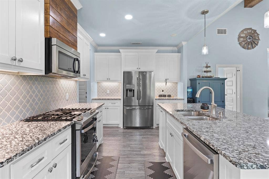 22477 County Road 2166, Troup, TX 75789 White cabinetry, stainless steel appliances, granite countertops, decorative tile backsplash, and wood-finish flooring