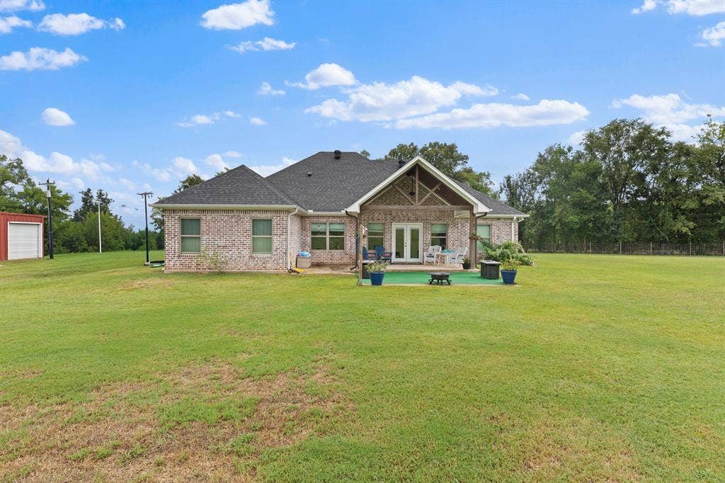 22477 County Road 2166, Troup, TX 75789 Expansive green lawn with a brick exterior, covered patio, double glass doors, and a detached storage building