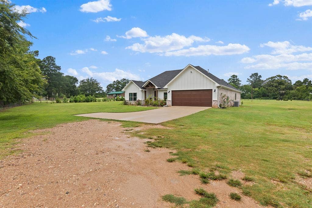 22477 County Road 2166, Troup, TX 75789 Single-story residence featuring white board and batten siding, brick accents, a dark shingled roof, and an attached brown garage door