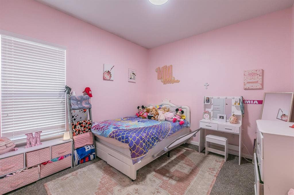 3020 Bella Lago Drive, Fort Worth, TX 76177 Bright secondary bedroom featuring soft pink walls, large windows with wood-finish flooring, and a neutral area rug