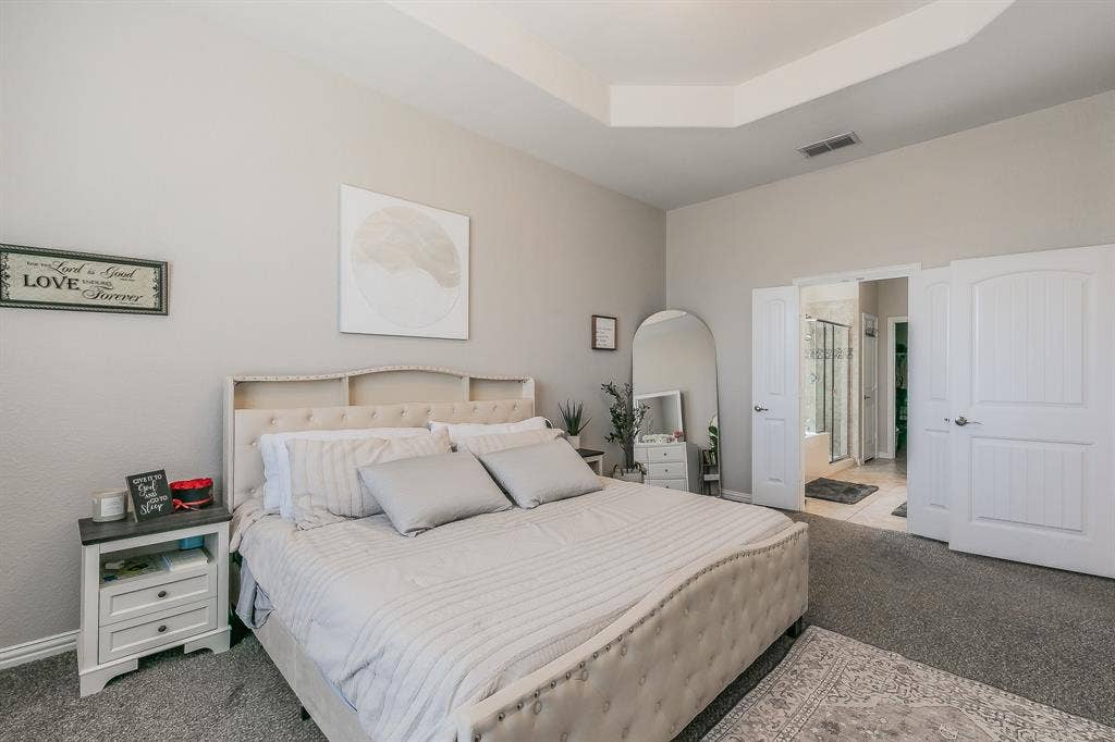 3020 Bella Lago Drive, Fort Worth, TX 76177 Primary bedroom featuring a upholstered bed frame with neutral bedding, carpeted flooring, dual nightstands with storage, arched mirror, and abundant natural light from multiple windows