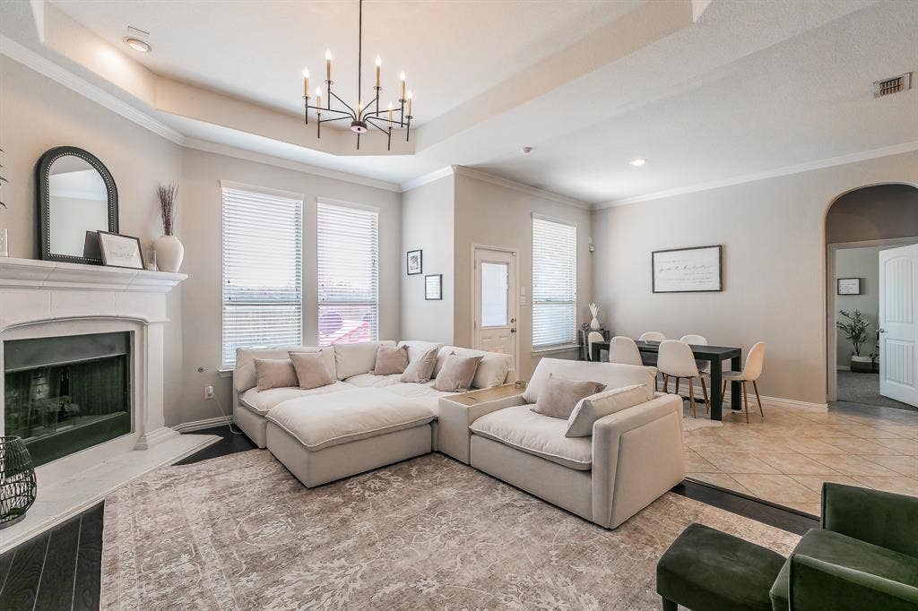 3020 Bella Lago Drive, Fort Worth, TX 76177 Living area featuring a tray ceiling, a fireplace with a stone mantel, multiple windows with blinds, a modern chandelier, and a tiled dining area