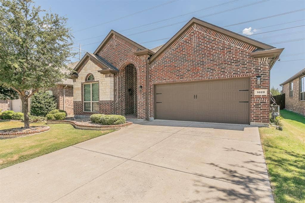 3020 Bella Lago Drive, Fort Worth, TX 76177 Brick and stone facade, arched entryway, concrete driveway, attached garage, and manicured landscaping