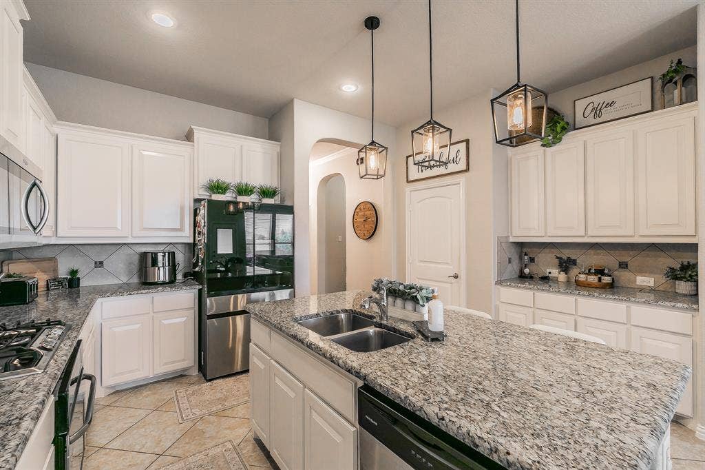 3020 Bella Lago Drive, Fort Worth, TX 76177 Kitchen featuring white cabinetry, light-toned granite countertops, a double basin sink, and pendant lighting