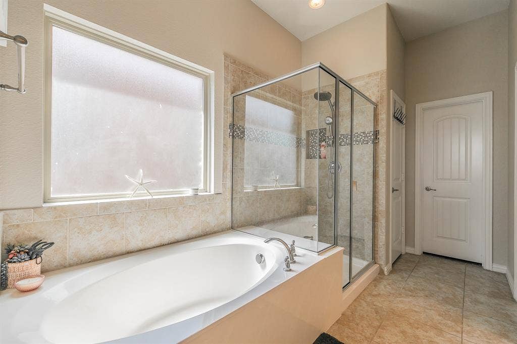 3020 Bella Lago Drive, Fort Worth, TX 76177 Soaking tub with deck-mounted faucet, walk-in glass shower enclosure, tiled shower surround with decorative accent band, and tiled flooring