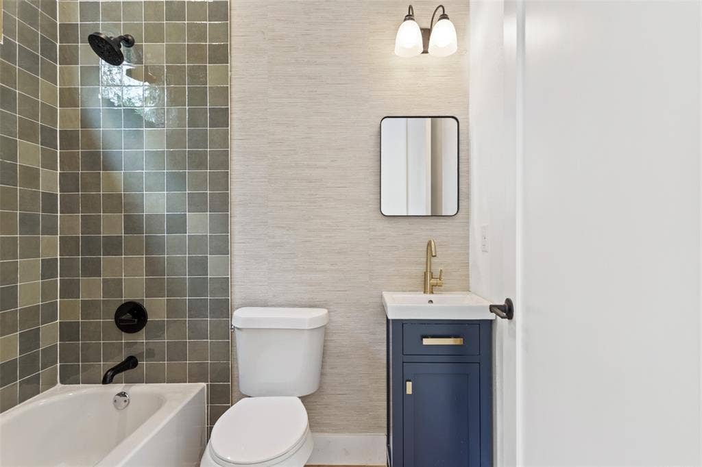 Bathroom featuring a bathtub with tile surround, toilet, vanity with integrated sink, and wall-mounted mirror