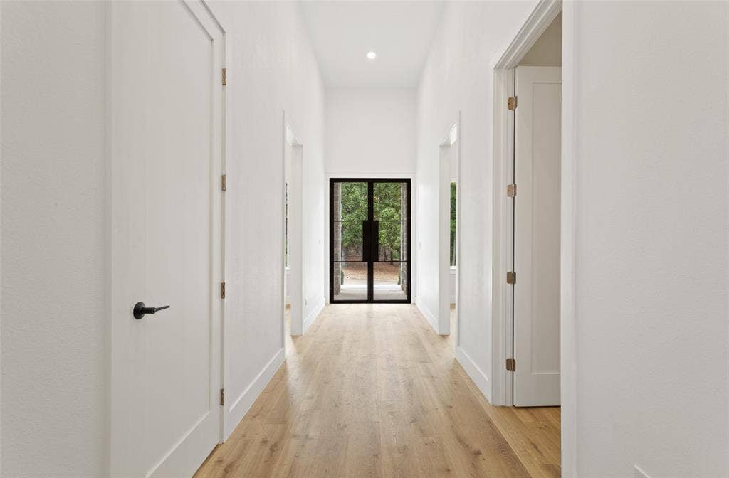 Hallway featuring wood-finish flooring, recessed lighting, white walls, and a black-framed glass door