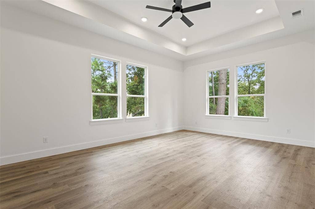 Tray ceiling featuring recessed lighting and a ceiling fan, complemented by wood-finish flooring and multiple windows