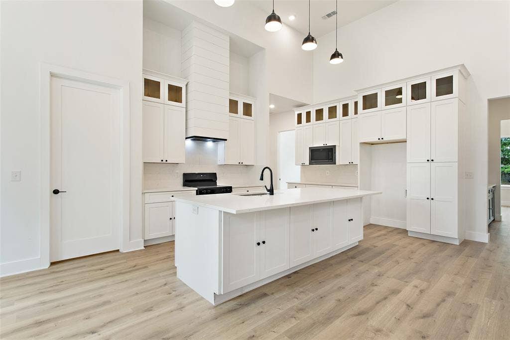 Vaulted ceilings, wood-finish flooring, white cabinetry with upper glass-front accents, and a large central island with an integrated sink