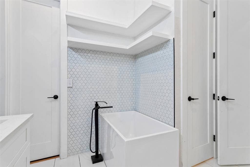 Freestanding soaking tub with a matte black floor-mounted faucet, alcove shelving, and patterned tile surround