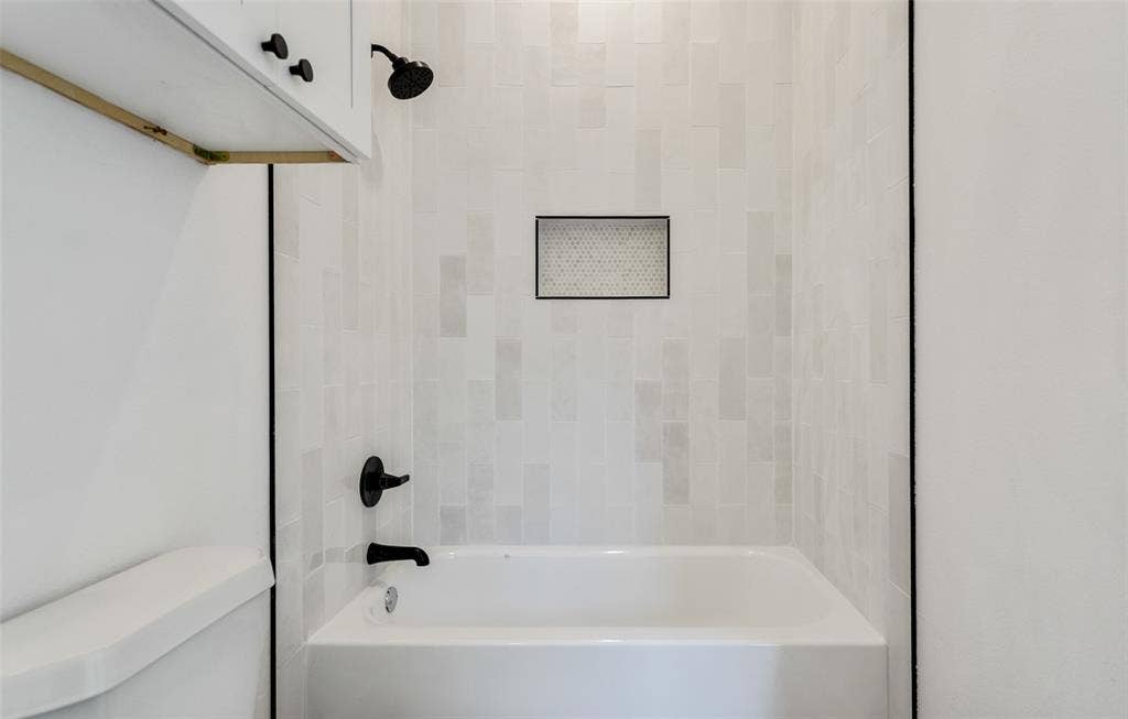 Bathtub with matte black fixtures, white subway tile surround, and a recessed shower niche