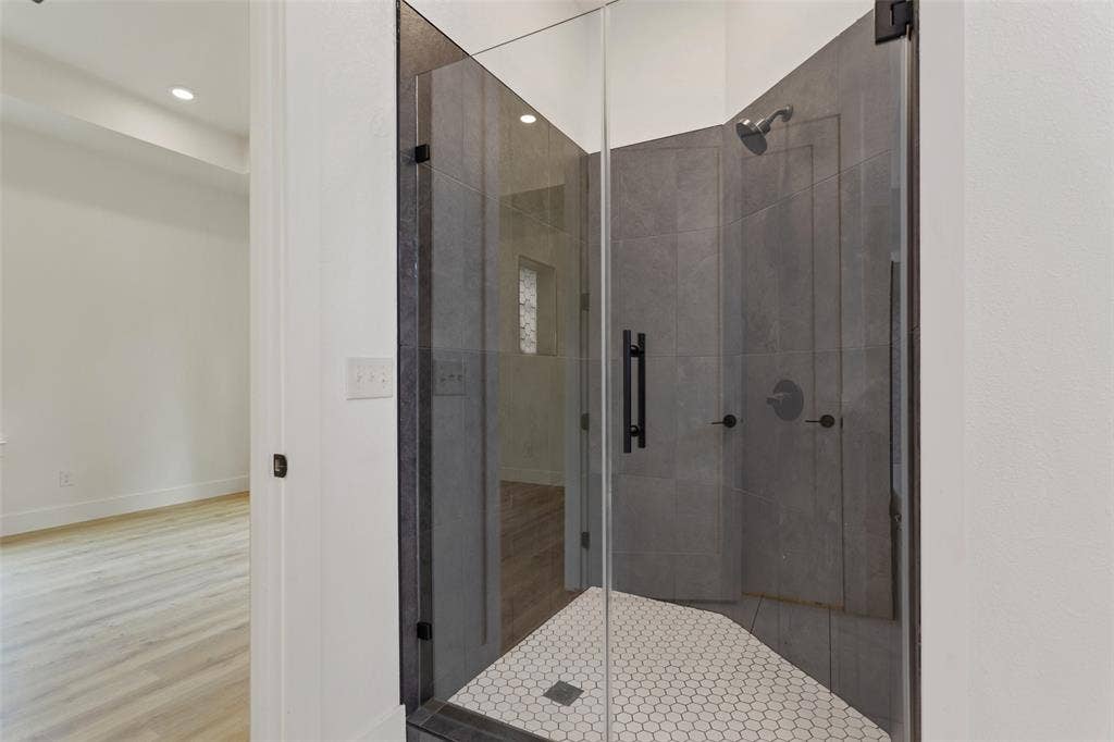 Glass-enclosed shower featuring large format wall tiles, a hexagon tile shower pan, and matte black fixtures