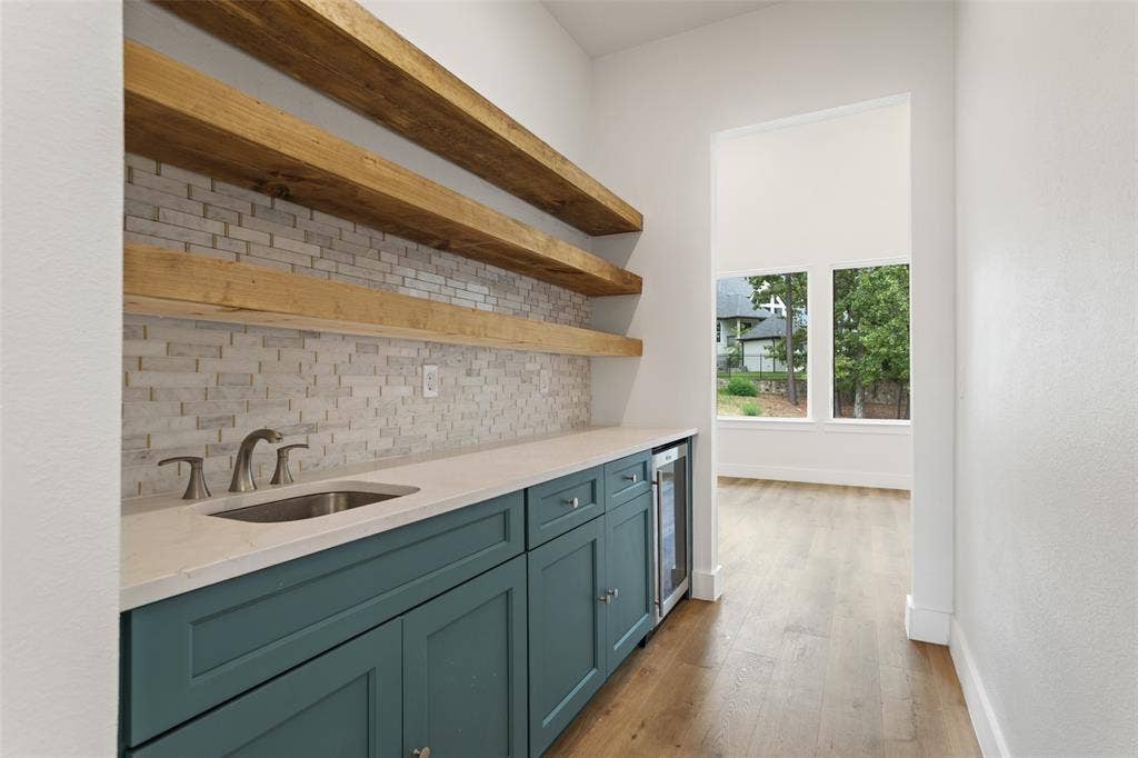 Wet bar featuring a rectangular undermount sink, quartz countertop, teal cabinetry, and a beverage cooler