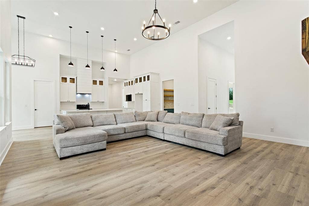 Vaulted ceilings, wood-finish flooring, recessed lighting, and a kitchen featuring a range hood with pendant lights and white cabinetry