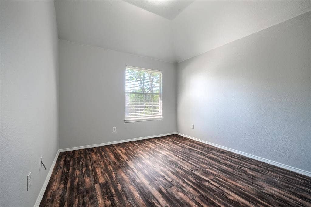 Vaulted ceiling, wood-finish flooring, white window blinds, and light gray wall paint