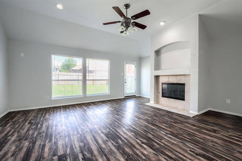 Vaulted ceilings with recessed lighting, wood-finish flooring, a fireplace with a tiled surround, a built-in arched alcove, and multiple windows